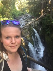smiling white woman with sunglasses standing in front of waterfall
