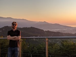 man in sunglasses standing in front of a sunset