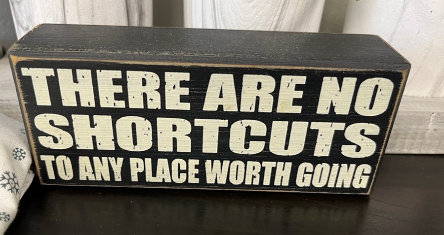 Image shows a plaque stating "There are no shortcuts to any place worth going".